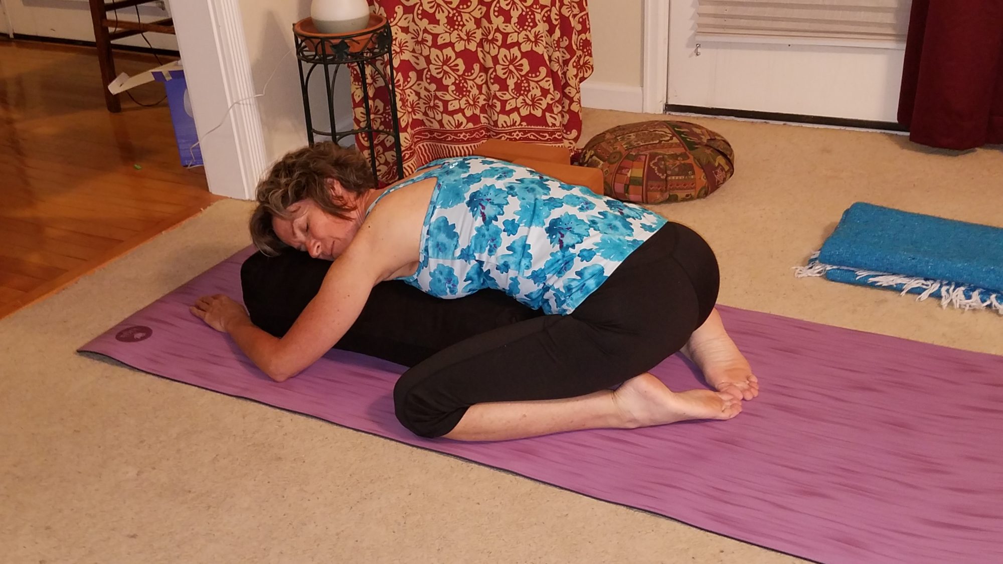 Woman resting on yoga bolster in supported child's pose.
